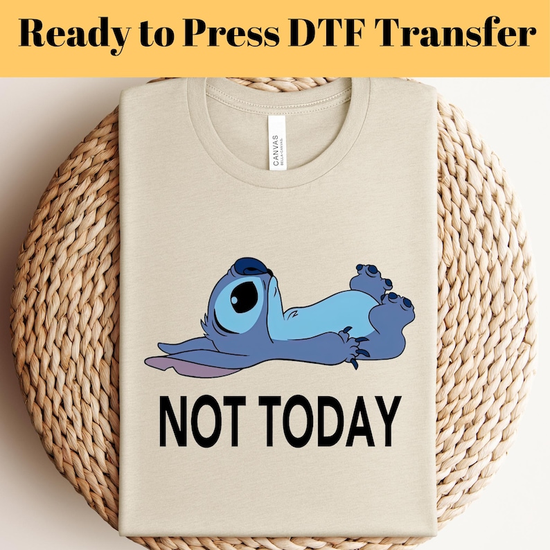 K&ouml;nnte beinhalten: Beiges T-Shirt mit einer Cartoonfigur in Blau und dem schwarzen Text &bdquo;NOT TODAY&ldquo;. Das T-Shirt liegt gefaltet auf einer gewebten Oberfl&auml;che. Der Text &bdquo;Ready to Press DTF Transfer&ldquo; steht oben.