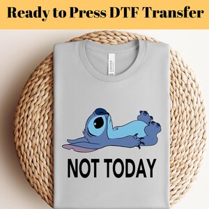 K&ouml;nnte beinhalten: Ein hellgraues T-Shirt mit einer Cartoonfigur in Blau- und Lilat&ouml;nen, die liegt. Der Text "NOT TODAY" ist darunter in Schwarz gedruckt. Die Worte "Ready to Press DTF Transfer" stehen oben.
