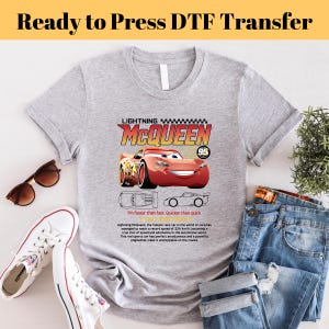 May include: A gray t-shirt with a red race car graphic. The car is red with black accents and has the words "Lightning McQueen" and "95" on it. The text below the car reads "I'm faster than fast. Quicker than quick." and includes a description of the car.