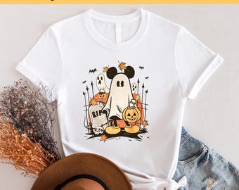 May include: White t-shirt featuring a graphic of Mickey Mouse dressed as a ghost holding a pumpkin. The graphic is in a vintage style with a black outline and orange and brown colours. The text "RIP" is on a tombstone in the background.