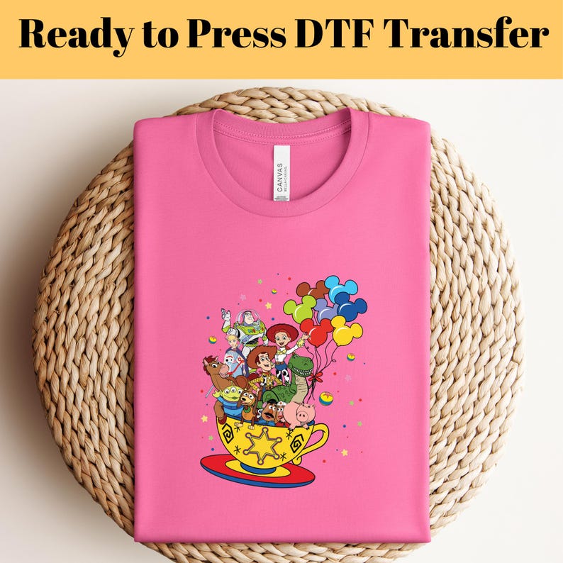 Pode incluir: Camiseta rosa com um gr&aacute;fico dos personagens do Toy Story em uma x&iacute;cara de ch&aacute; com bal&otilde;es. Os personagens incluem Woody, Buzz Lightyear, Jessie, Rex e Hamm. O texto "Ready to Press DTF Transfer" est&aacute; na parte superior da imagem.