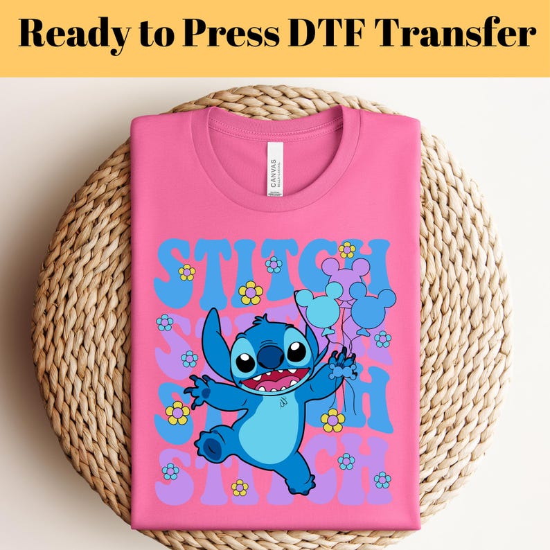 May include: Pink t-shirt with a blue Stitch character holding balloons with Mickey Mouse ears. The text "Stitch" is written in a retro font with flowers and purple accents.
