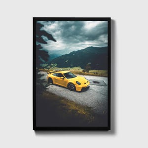 May include: A yellow sports car driving on a winding road through a mountain pass. The car is surrounded by green trees and a cloudy sky.