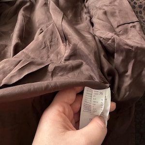 May include: A brown jacket interior with a tag showing size 36. The jacket's lining is a smooth, dark brown fabric. The tag displays size and material information. The jacket is hanging on a white hanger.