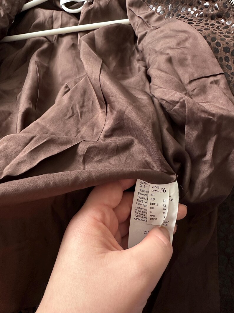 May include: A brown jacket interior with a tag showing size 36. The jacket's lining is a smooth, dark brown fabric. The tag displays size and material information. The jacket is hanging on a white hanger.