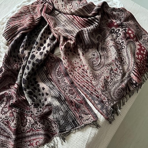 May include: A long, rectangular scarf with a paisley pattern in shades of burgundy, brown, and beige. The scarf has a fringe on the ends.