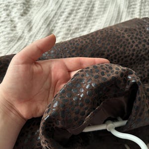 May include: Brown jacket with a dark spotted pattern. The jacket is hanging on a white hanger. The interior lining is a solid brown color.