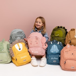 Könnte beinhalten: Eine Auswahl an Kinderrucksäcken mit Tiermotiven, darunter Löwe, Dinosaurier und Katze. Die Rucksäcke sind in Pastelltönen wie Rosa, Gelb und Blau gehalten. Einige haben personalisierte Namen.