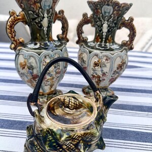May include: A set of three vintage ceramic vases and a teapot. The vases are decorated with floral patterns and have ornate handles. The teapot is shaped like a seashell and has a lid with a seashell finial.