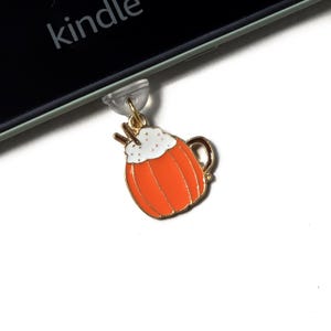 Könnte beinhalten: Ein goldfarbener Anhänger in Form eines orangefarbenen Pumpkin Spice Latte mit weißer Schlagsahne und zwei braunen Strohhalmen. Der Anhänger ist an einem transparenten Kunststoffteil befestigt, im Hintergrund ist das Wort "kindle" zu sehen.