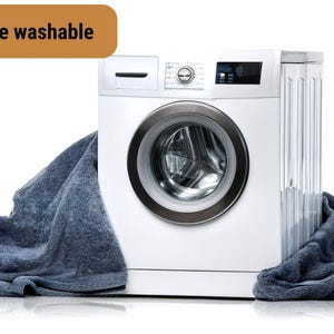 Puede incluir: Una lavadora blanca con una toalla azul drapeada sobre ella. La lavadora tiene una puerta plateada con una abertura redonda. El texto "Machine washable" es visible en la esquina superior izquierda de la imagen.
