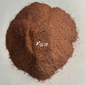 Puede incluir: Primer plano de un montón de posos de café marrón oscuro. Los posos están finamente molidos y tienen un tono ligeramente rojizo. El texto "@JP" es visible en el centro de la imagen.