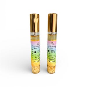 May include: Two glass cologne bottles with gold-coloured caps. Each bottle has a label with text including "JEHOVAH" and "ALIGNMENT COLOGNE". The bottles contain a clear liquid and small, beige-coloured pieces at the bottom.