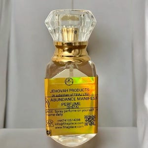 Puede incluir: Frasco de perfume de vidrio transparente con cuello dorado y tapón facetado en forma de cristal. La etiqueta dice "ABUNDANCE MANIFEST PERFUME (SHEFA)" e incluye información de contacto. El frasco está diseñado para uso diario.