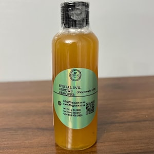 May include: A clear glass bottle with a yellow liquid inside. The bottle has a black cap and a green and silver label that reads "SPECIAL EVIL ARROWS REMOVER (Very powerful 100%". The label also includes contact information and a QR code.