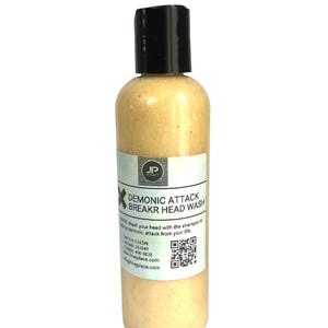 May include: A cylindrical bottle of head wash with a black cap. The label reads "DEMONIC ATTACK BREAKR HEAD WASH" with additional text and a QR code. The liquid inside is a light beige color.