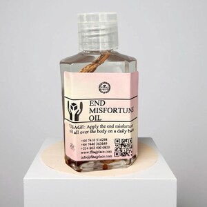 May include: A clear glass bottle with a clear plastic cap, containing a brown stick and oil. The label reads "END MISFORTUNE OIL" with usage instructions and contact information. The bottle is on a white surface.