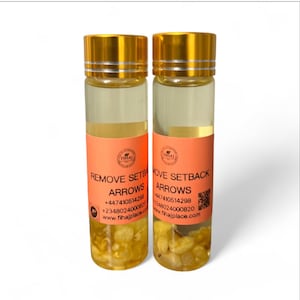 Op de afbeelding: Twee glazen flessen met goudkleurige doppen en oranje etiketten. De etiketten lezen "REMOVE SETBACK ARROWS" en bevatten contactgegevens. De flessen bevatten een gele vloeistof en kleine, lichtgekleurde vaste stoffen.