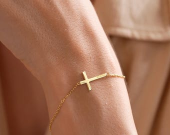 May include: A gold cross charm bracelet with a delicate chain. The cross is simple and elegant, with a small inscription on the back.