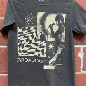Könnte beinhalten: Ein schwarzes T-Shirt mit einem Vintage-Grafikdesign, das eine Person zeigt, die in ein Mikrofon singt, ein Schachbrettmuster, einen Stern, einen Fuß und das Wort "BROADCAST".