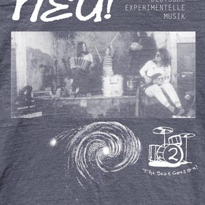 May include: A charcoal gray t-shirt featuring a white graphic print. The design includes the text "neu! DEUTSCHE EXPERIMENTELLE MUSIK," a black and white photograph of a band, a spiral galaxy illustration, a drum kit icon with a "2," and "The Beat Goes on!"