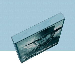 May include: A light blue box with a black and white portrait of a man in a hat. The box has the words "Pale Rider" and other text. The box is angled, showing the top and side.