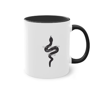 Può includere: Tazza in ceramica bianca con bordo e manico neri. La tazza presenta una silhouette nera di un serpente con il testo "Look What You Made Me Brew" in un carattere gotico grigio.