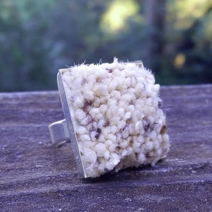 May include: A white and brown textured ring with a silver band. The ring is square shaped and has a fuzzy texture.
