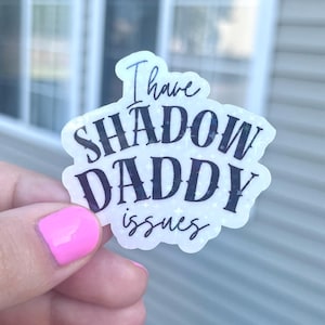 May include: A white sticker with black text that reads "I have shadow daddy issues" with a glittery background.