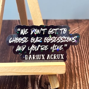 May include: A black and white sticker with a quote from the book "A Court of Thorns and Roses" by Sarah J. Maas. The quote reads: "We don't get to choose our obsessions and you're mine." The quote is attributed to "DARIUX ACRUX".
