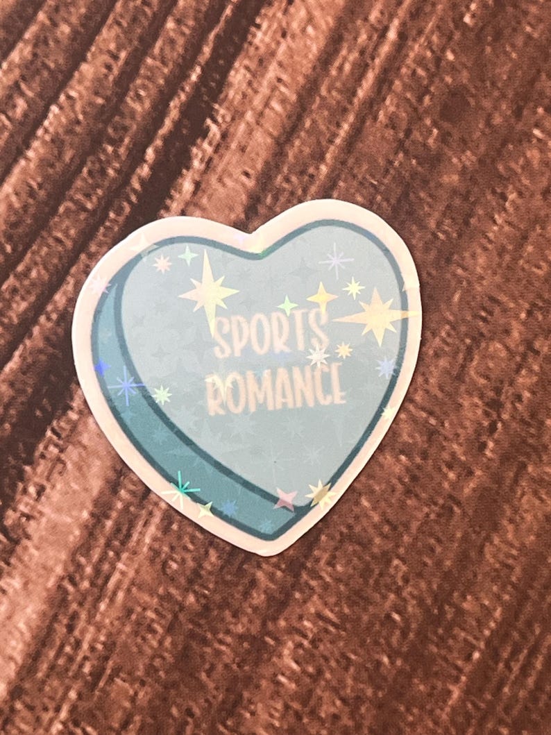 May include: A blue heart-shaped sticker with a holographic finish. The sticker has the text "SPORTS ROMANCE" in white letters.