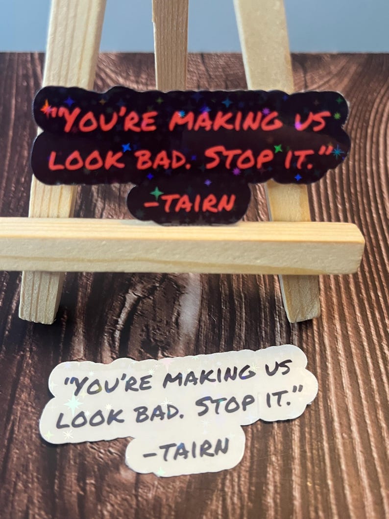 Puede incluir: Dos pegatinas con fondo negro y purpurina iridiscente. El texto en las pegatinas dice "You're making us look bad. Stop it." y est&aacute; escrito en blanco, con una fuente de letra manuscrita. El texto "TAIRN" est&aacute; escrito en rojo debajo del texto principal.