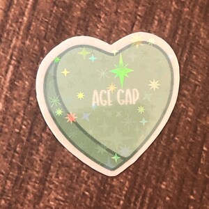 May include: A green heart-shaped sticker with a glittery finish and the text "AGE GAP" in white.