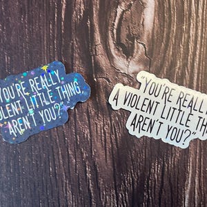 Pode incluir: Dois adesivos com o texto "You're really a violent little thing, aren't you?" Um adesivo &eacute; preto com glitter prata e o outro &eacute; prata com texto preto.