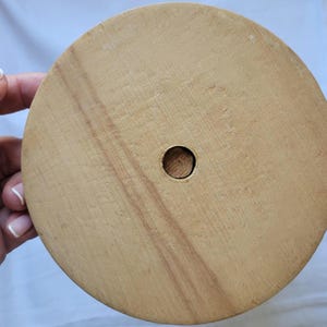 Puede incluir: Una base redonda de madera con un agujero en el centro. La base es de color marr&oacute;n claro y tiene una superficie lisa.