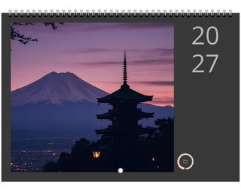 Peut inclure: Un calendrier mural pour l'année 2027 avec une reliure à spirale sur le dessus. L'image montre la silhouette d'une pagode à plusieurs niveaux sur un ciel de coucher de soleil violet et rose avec une grande montagne et le texte 20 27.