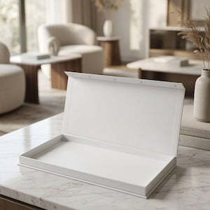 Pode incluir: Uma caixa retangular branca com uma tampa articulada aberta, revelando um interior plano e vazio. A caixa apresenta uma superfície limpa e lisa e um design estruturado com uma tira de fecho magnético visível na borda superior da tampa.