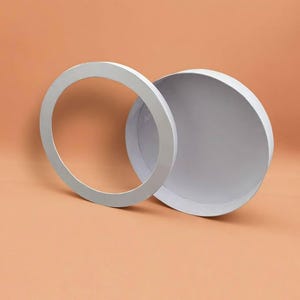 Può includere: Una scatola regalo rotonda bianca con un coperchio separato dotato di un'apertura circolare. La scatola ha una finitura opaca liscia e una struttura pulita. Il coperchio è posizionato verticalmente, appoggiato contro la base del contenitore.
