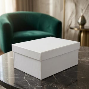 Puede incluir: Una caja rectangular blanca con tapa, que presenta un acabado liso y mate. La caja está construida con bordes limpios y definidos y un diseño sencillo de color sólido, ofreciendo una apariencia uniforme en todos los lados visibles.