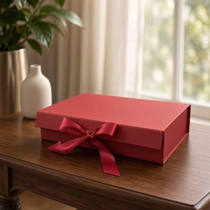 Könnte beinhalten: Eine rechteckige rote Geschenkbox mit Klappdeckel und einem passenden roten Satinband, das vorne zu einer Schleife gebunden ist. Die Box hat eine glatte, matte Oberfläche und ist horizontal ausgerichtet, was ihre klaren Kanten betont.