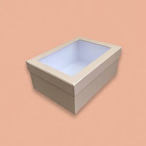 May include: A rectangular beige cardboard box with a clear plastic window on the lid. The box features a solid light-colored exterior and a white interior lining, providing a clean and simple structure for storage or display purposes.