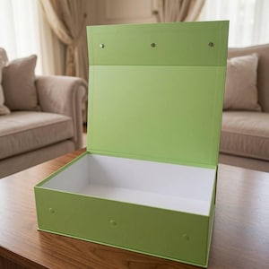 May include: A rectangular lime green storage box with an open hinged lid. The exterior is a solid matte lime green, while the interior is white. Three small circular magnetic closures are visible along the front edge and the top lid flap.
