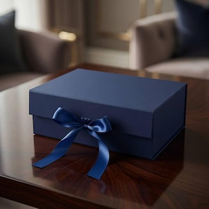 Op de afbeelding: Een rechthoekige marineblauwe geschenkdoos met een matte afwerking, voorzien van een bijpassend marineblauw satijnen lint gestrikt aan de voorzijde. De doos heeft een gestructureerd ontwerp met een scharnierend deksel en een glad, effen oppervlak.