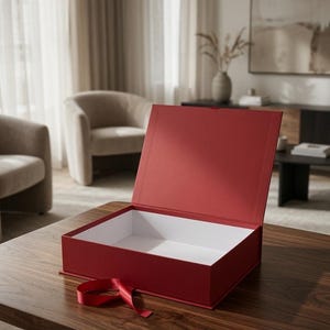 Op de afbeelding: Een rechthoekige geschenkdoos met een dieprode buitenkant en een witte binnenkant. De doos heeft een openstaand scharnierend deksel en een bijpassend rood lint aan de voorzijde voor sluiting, geplaatst op een vlakke ondergrond.