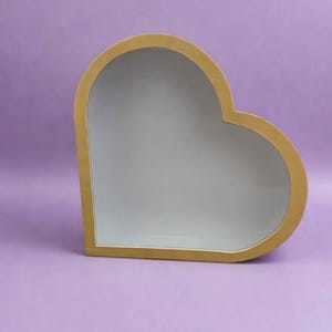Pode incluir: Uma caixa de sombra em forma de coração com uma moldura de madeira clara e lisa e um painel traseiro interior branco liso. A estrutura apresenta um design profundo com frente aberta e bordas arredondadas e limpas, oferecendo uma visão clara da superfície branca.