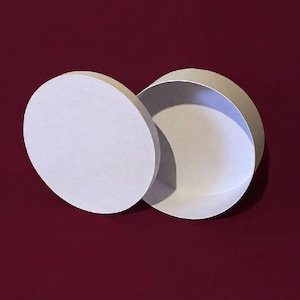Peut inclure: Boîte ronde en carton blanc, ouverte, avec son couvercle. Le couvercle est légèrement décalé, révélant l'intérieur de la boîte. L'arrière-plan est rouge foncé.