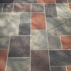 May include: A stone patio surface composed of rectangular and square tiles in varying shades of terracotta, charcoal gray, and sage green. The tiles feature a textured, natural finish with visible grout lines separating each individual stone piece.