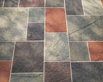 May include: A stone patio floor featuring a multi-sized rectangular and square tile pattern. The tiles display a textured, weathered surface in varied shades of terracotta red, slate gray, and muted sage green, separated by thin, light-colored grout lines.