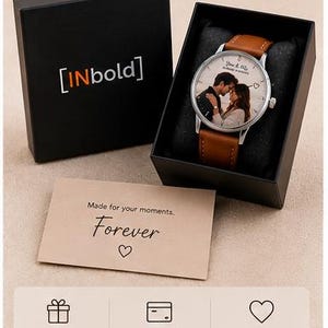 May include: A personalized watch with a brown leather strap and a silver-tone case. The watch face features a couple's photo and the words "Forever" and "Made for your moments" are printed on a card. The watch is presented in a black gift box.