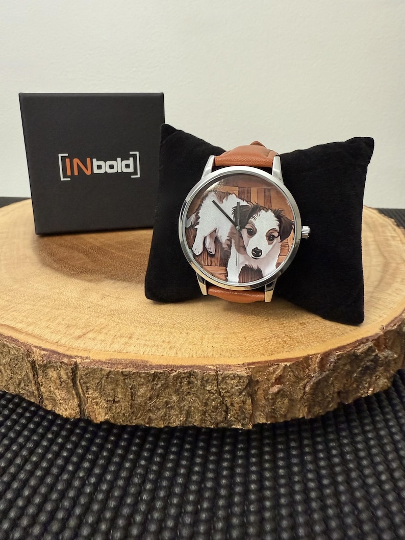 May include: A wristwatch with a brown leather band and a silver-colored case. The watch face features a color image of a puppy. A black box with the text "[INbold]" is visible in the background.